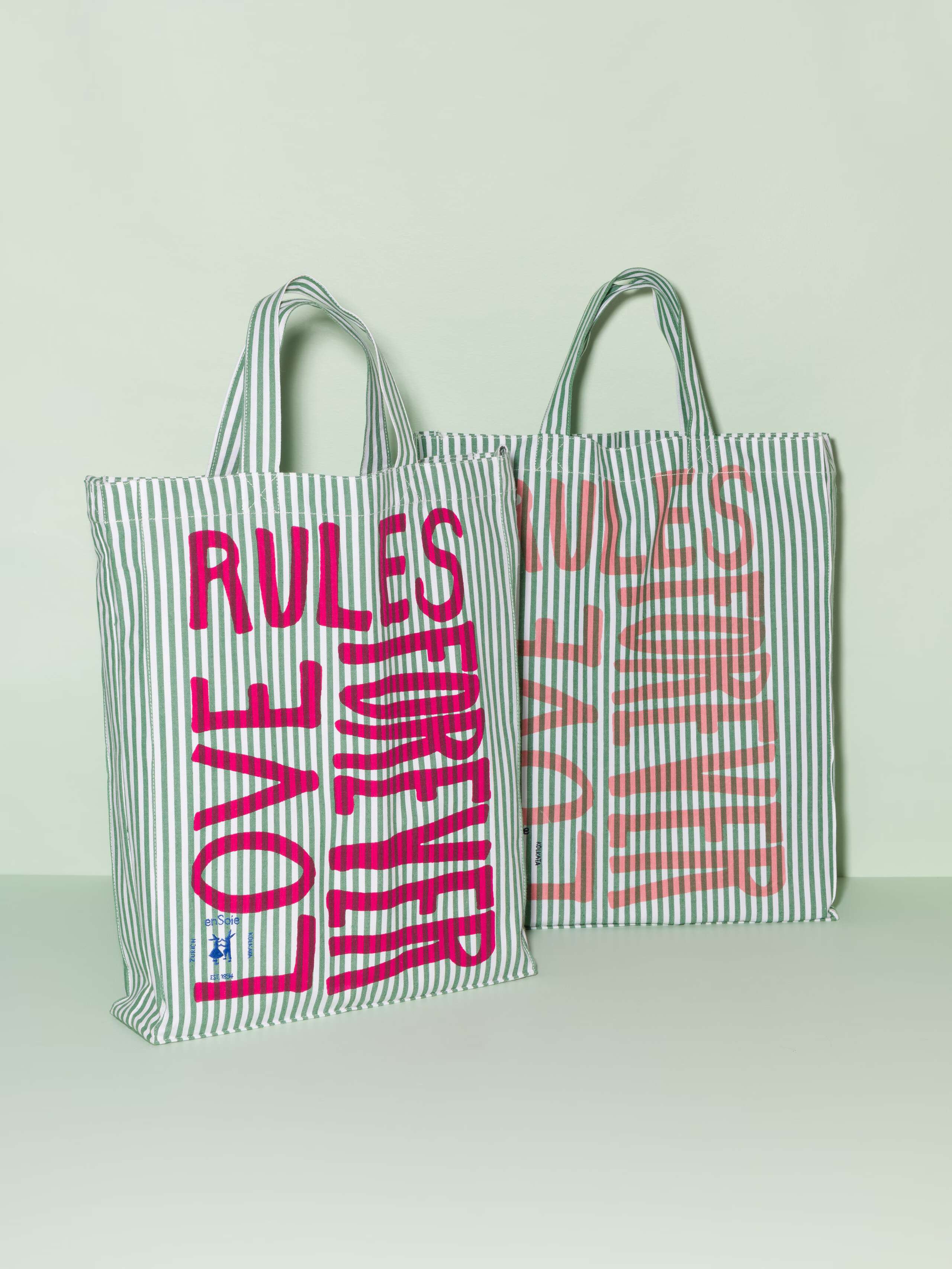 Two cotton tote bags with a green stripe pattern and a pink and coral print that says "Love rules forever"