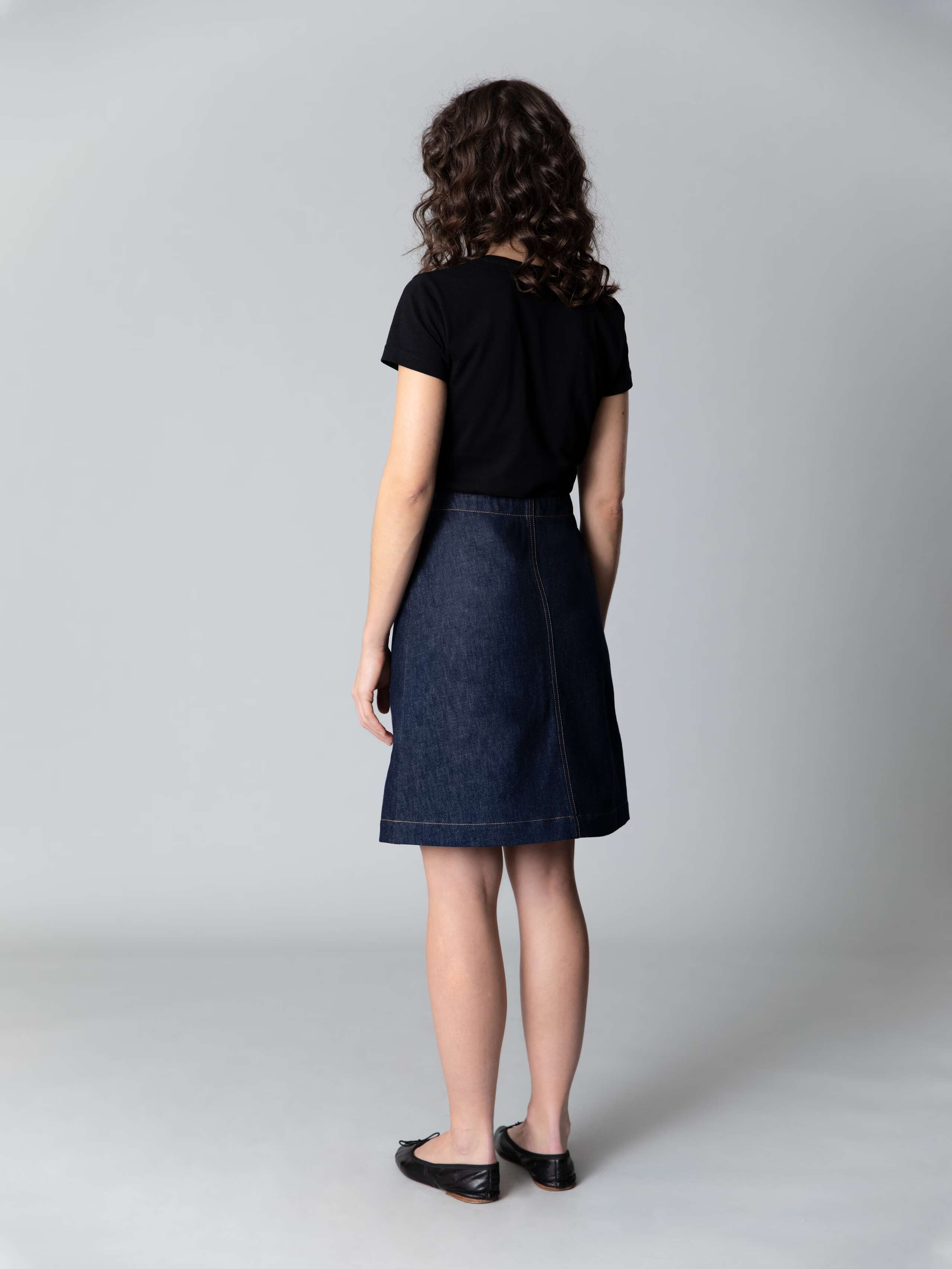 Model is wearing a beautiful a-line denim skirt combined with a black shirt and black ballerina flats
