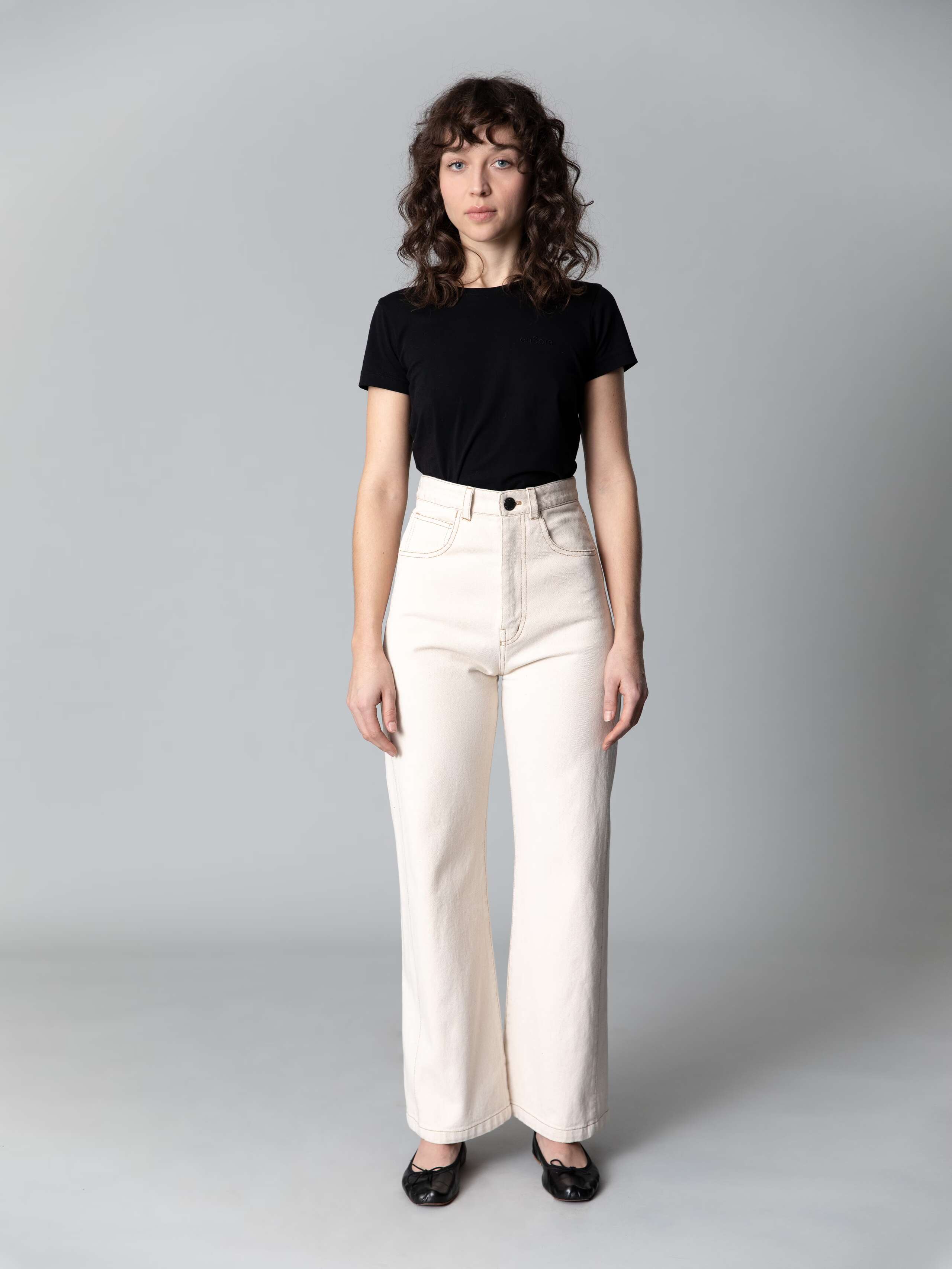 Model with dark hair, blue eyes and light skin is wearing a black cotton shirt and beautiful high waist jeans in a ecru colour