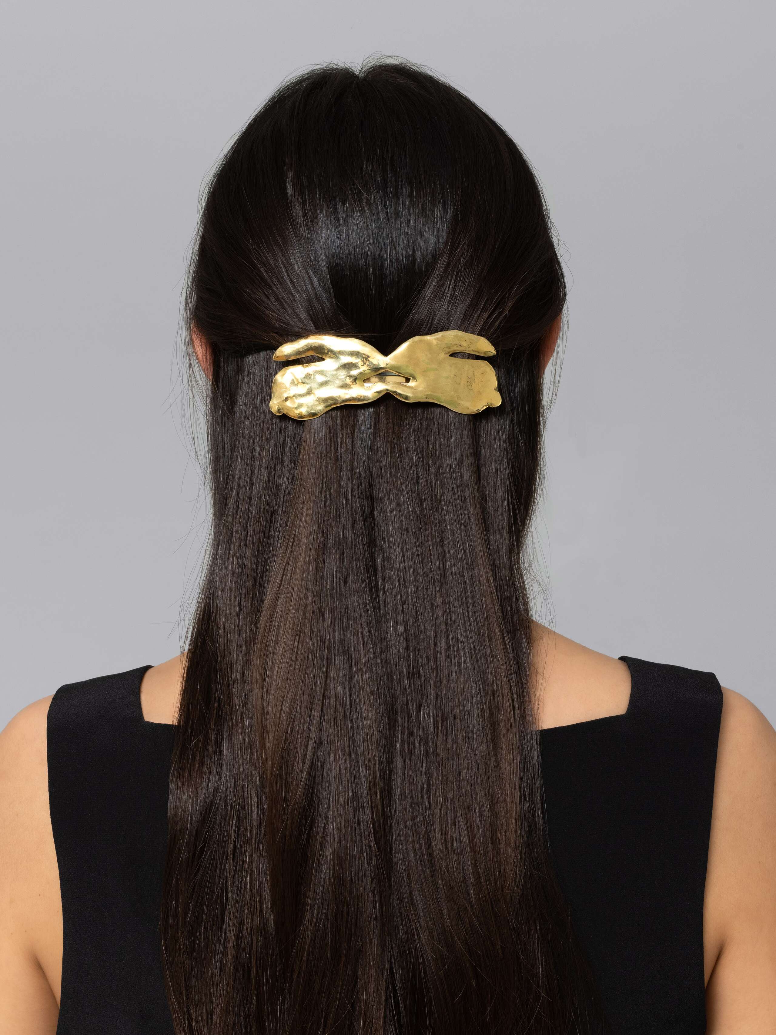 Women with dark brown hair is wearing a beautiful brass hair clip in the shape of two rabbits
