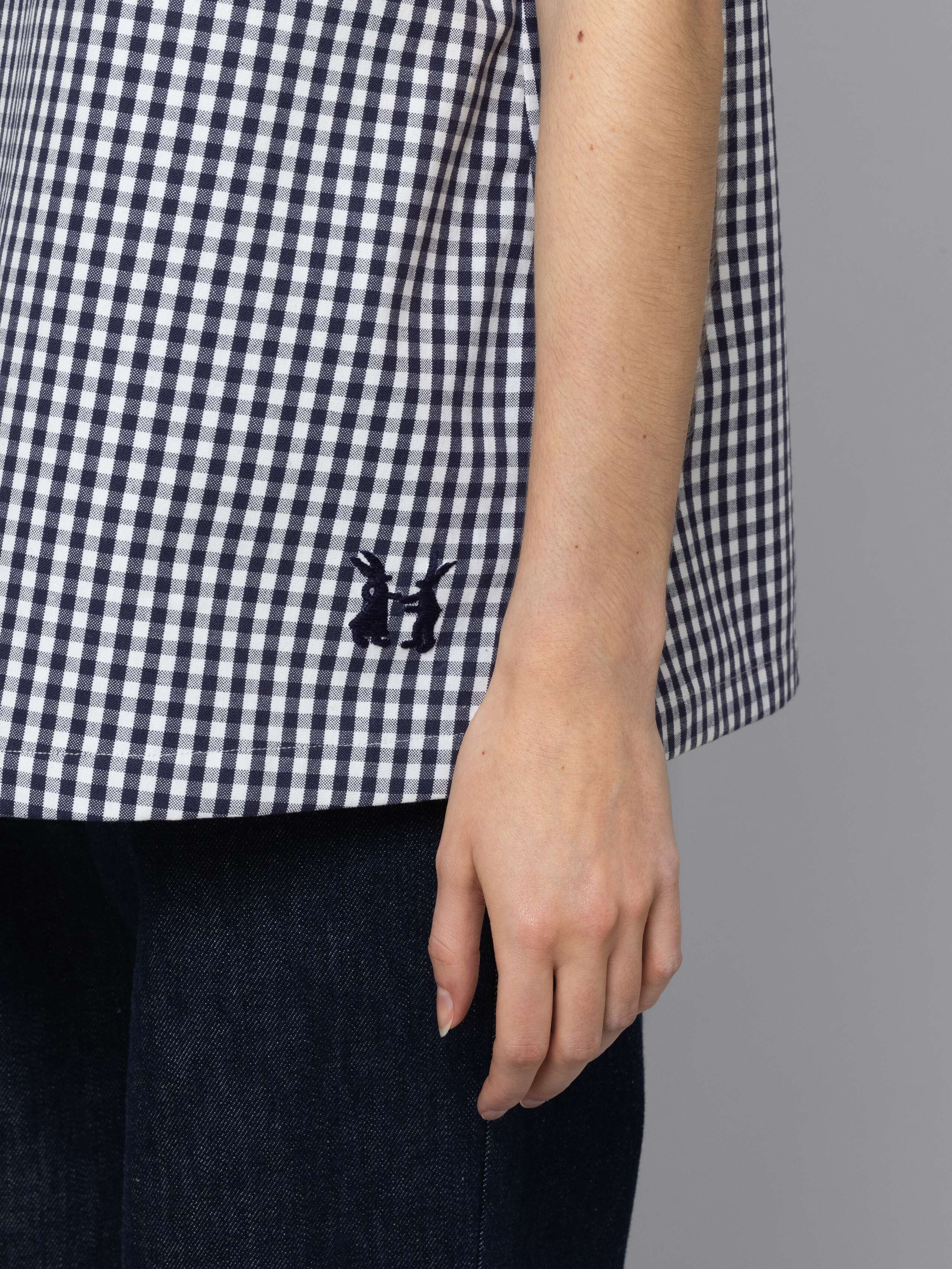 Female model is wearing a an airy long top featuring a beautiful navy vichy check pattern