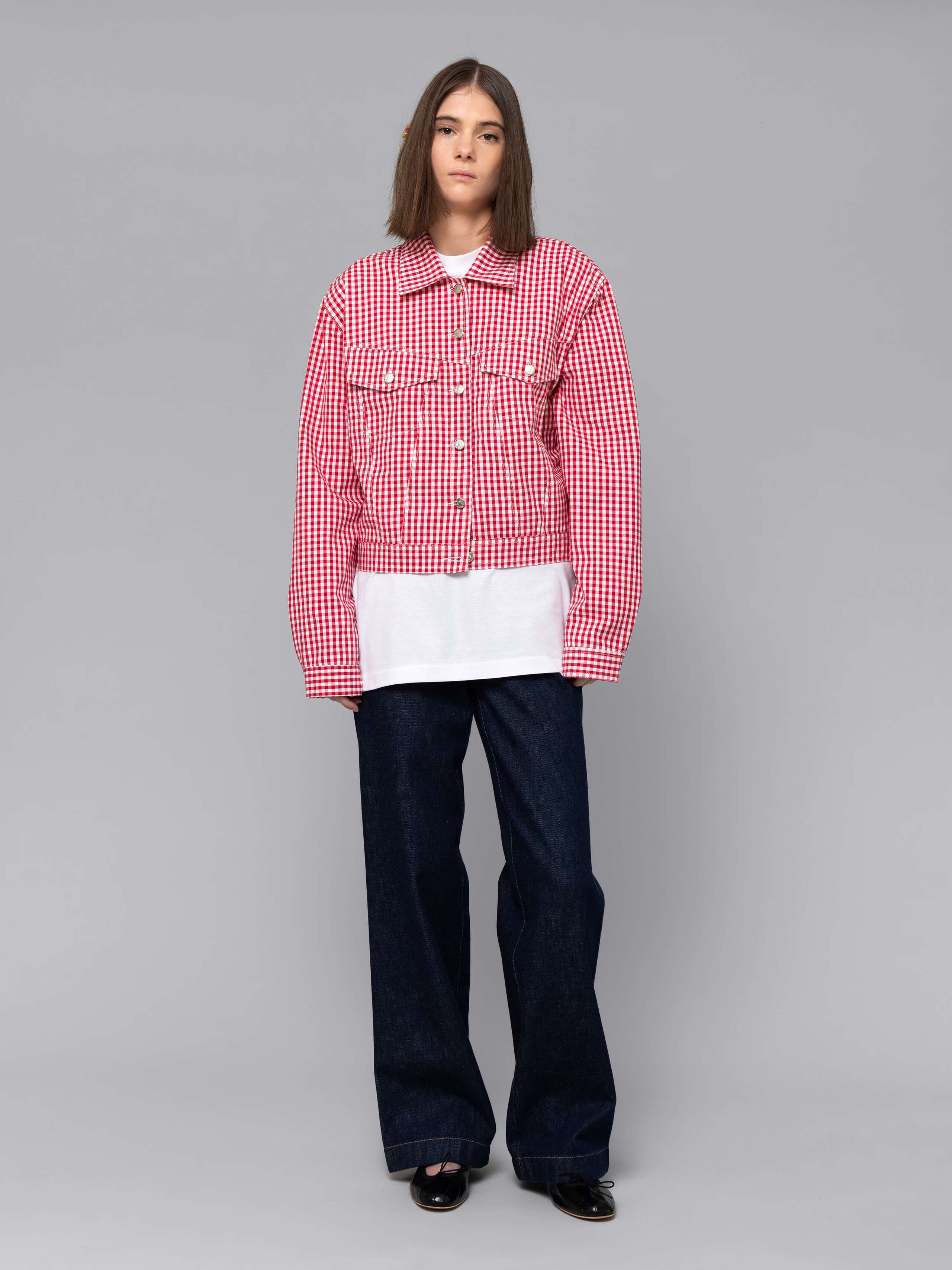 Female model is wearing a a boxy denim trucker jacket featuring a beautiful red vichy check pattern