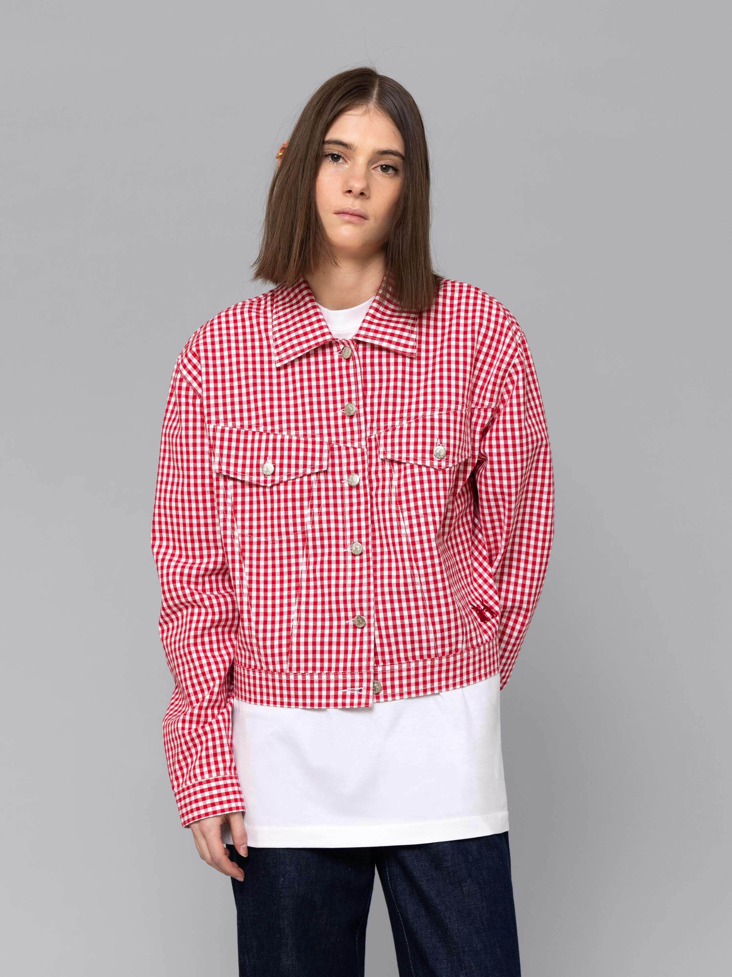 Female model is wearing a a boxy denim trucker jacket featuring a beautiful red vichy check pattern