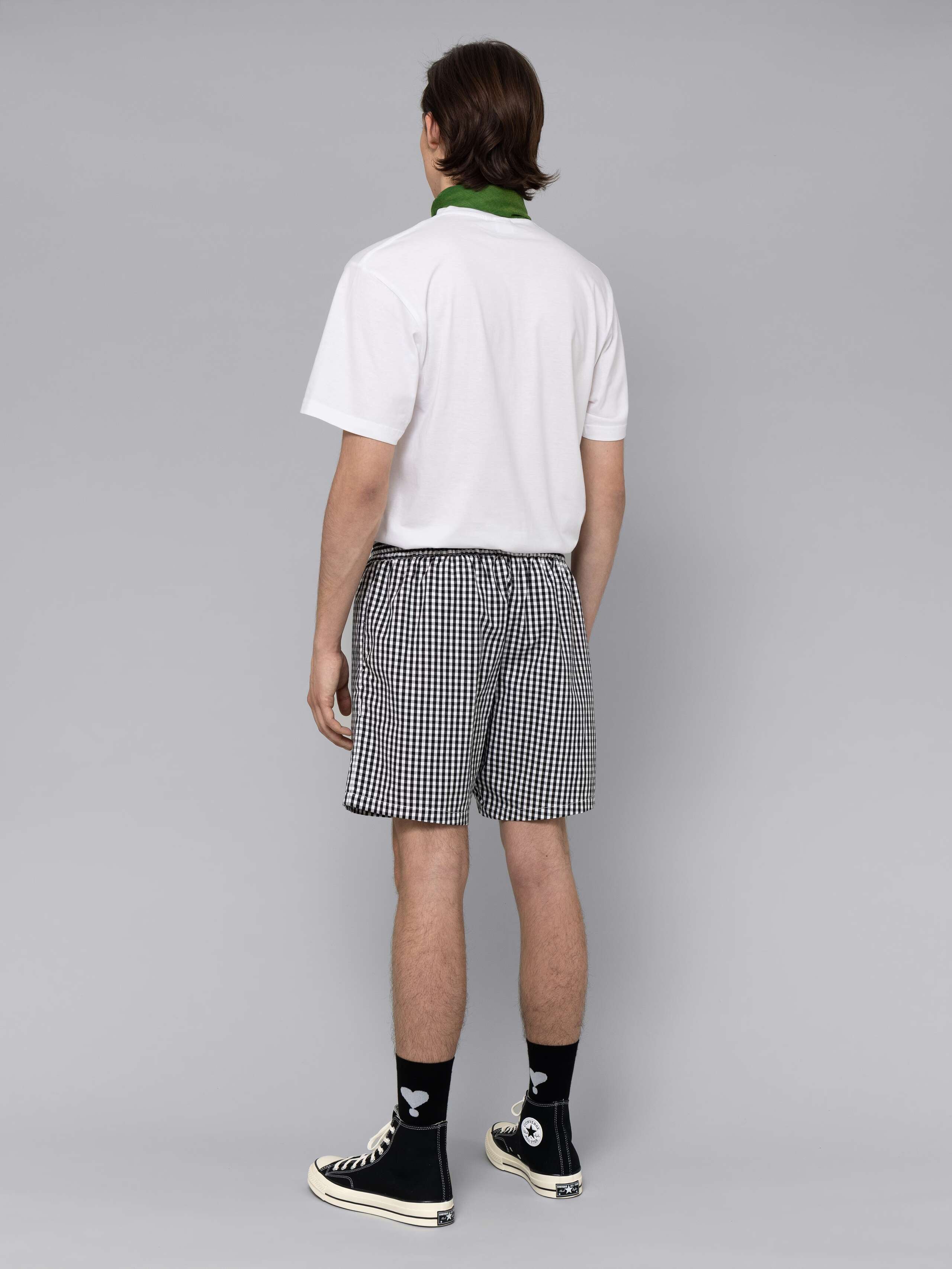 Male model is wearing a summery combination of a cotton short featuring a black vichy check pattern and a white t-shirt