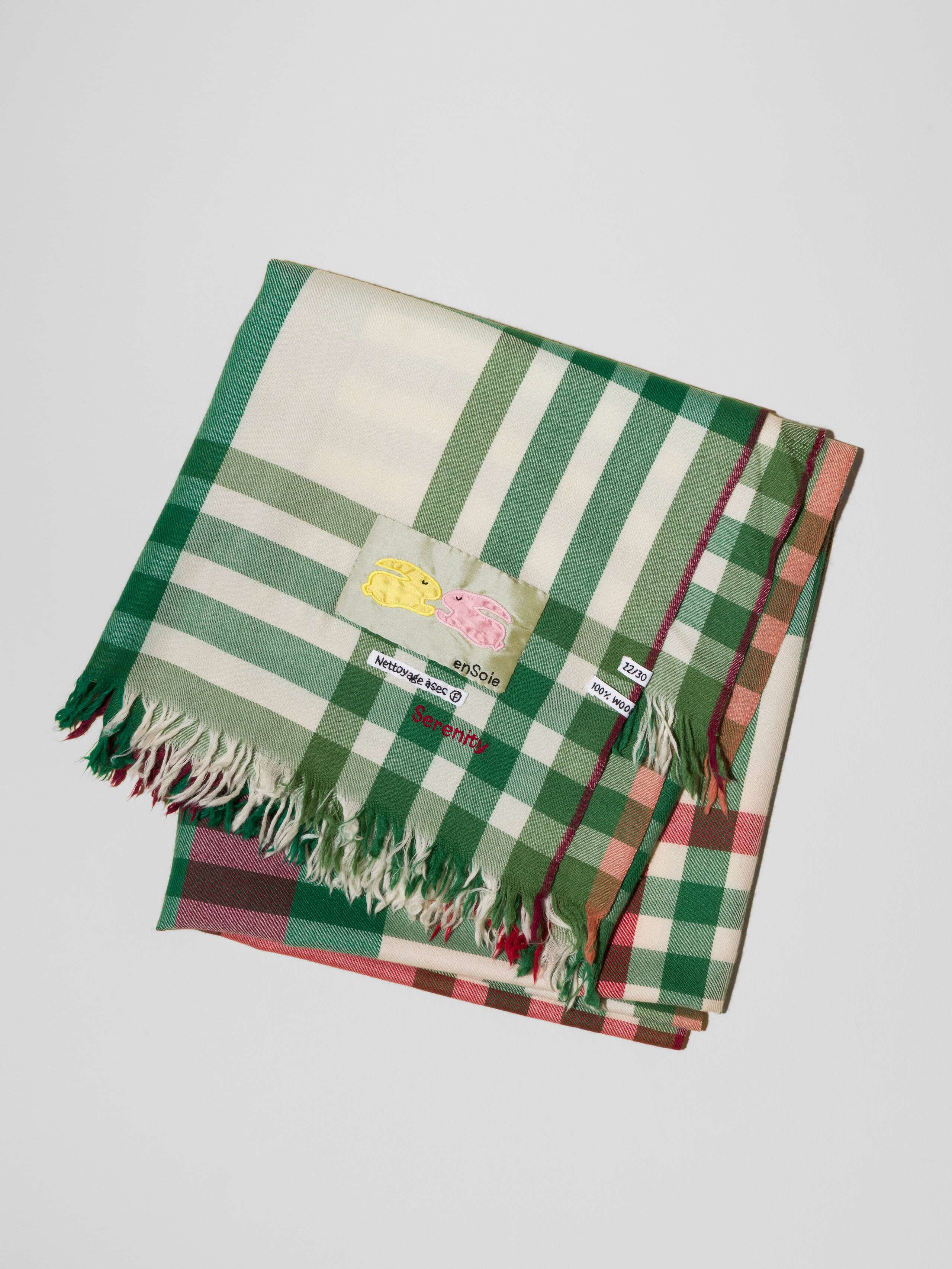 Picture of a detail of a wool scarf in a light beige shade featuring a green and red check pattern