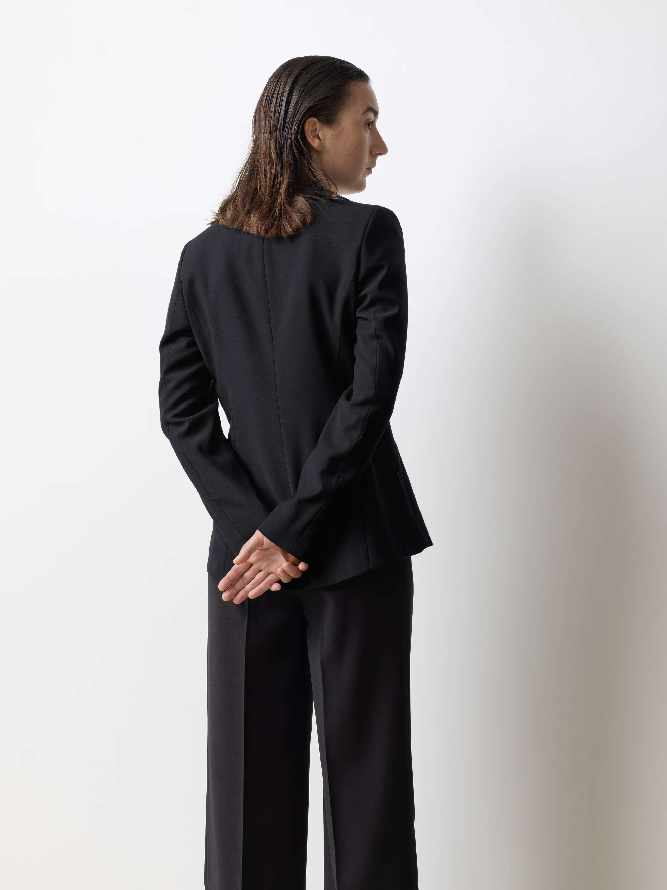 Picture of a female model wearing a black cool wool blazer in combination with matching pants and a brown shiny silk blouse 