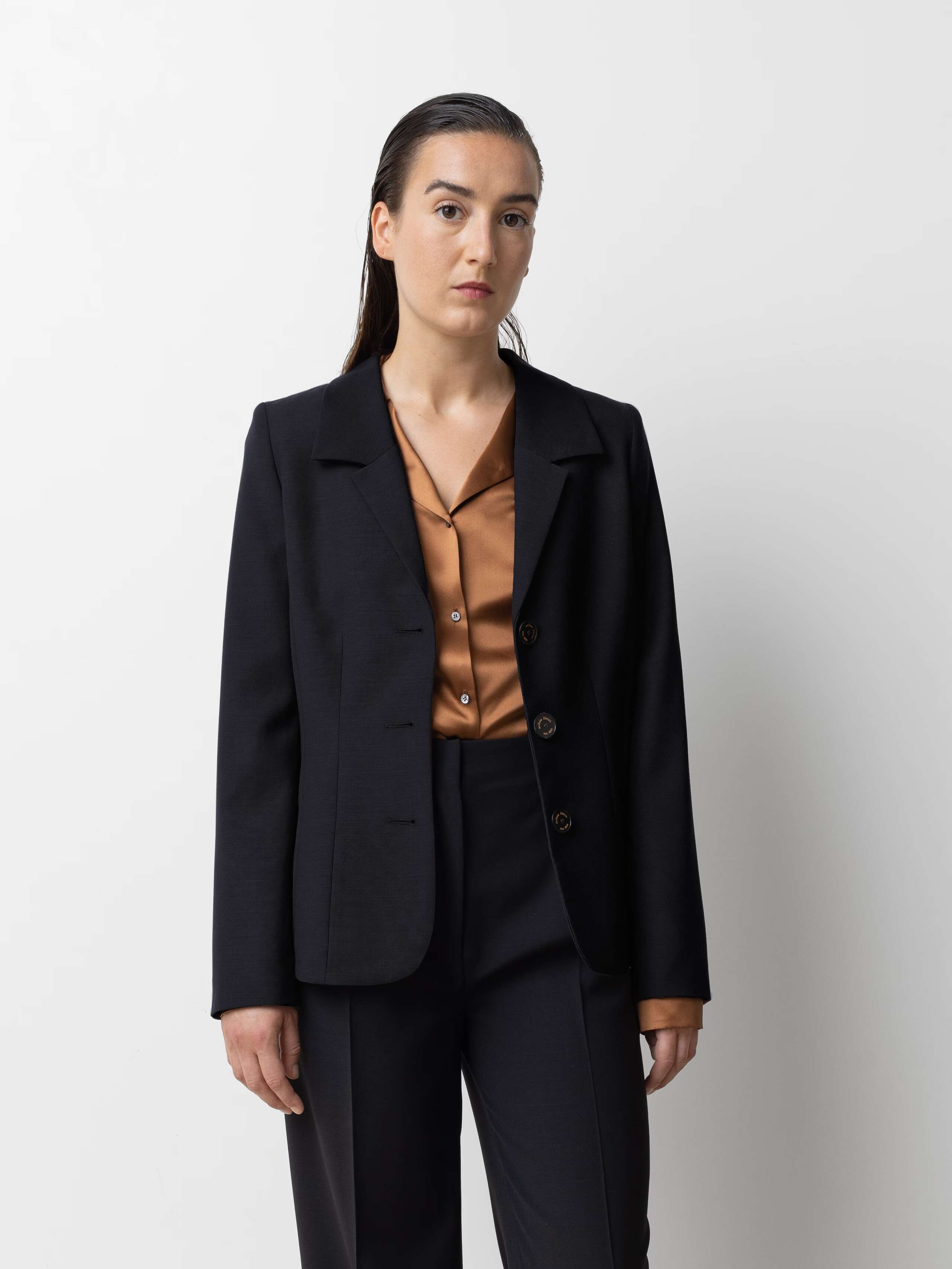 Picture of a female model wearing a black cool wool blazer in combination with matching pants and a brown shiny silk blouse 