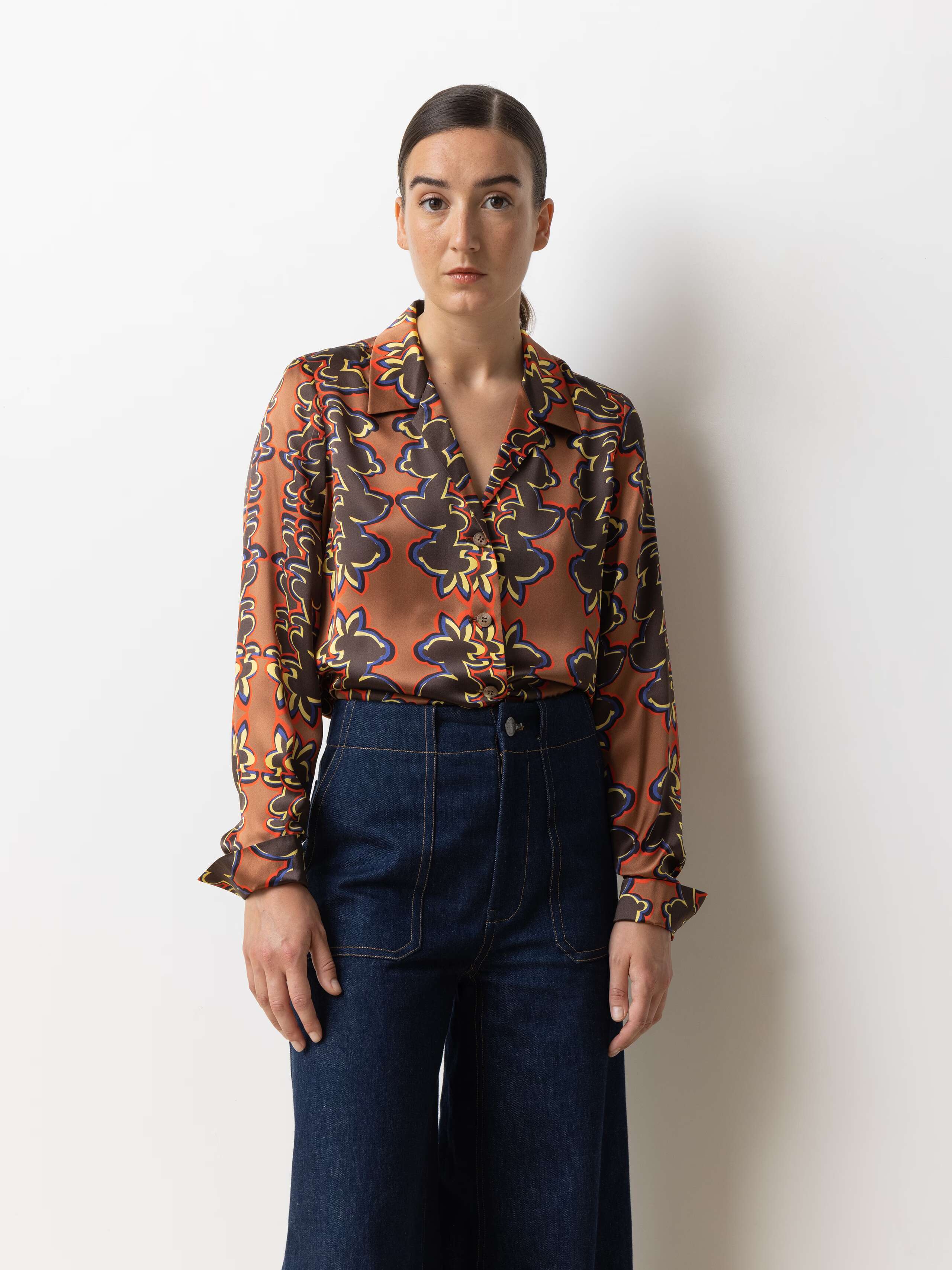 Picture of a model wearing a silk blouse in warm shades of brown, red and yellow in combination with a classic bleu jeans