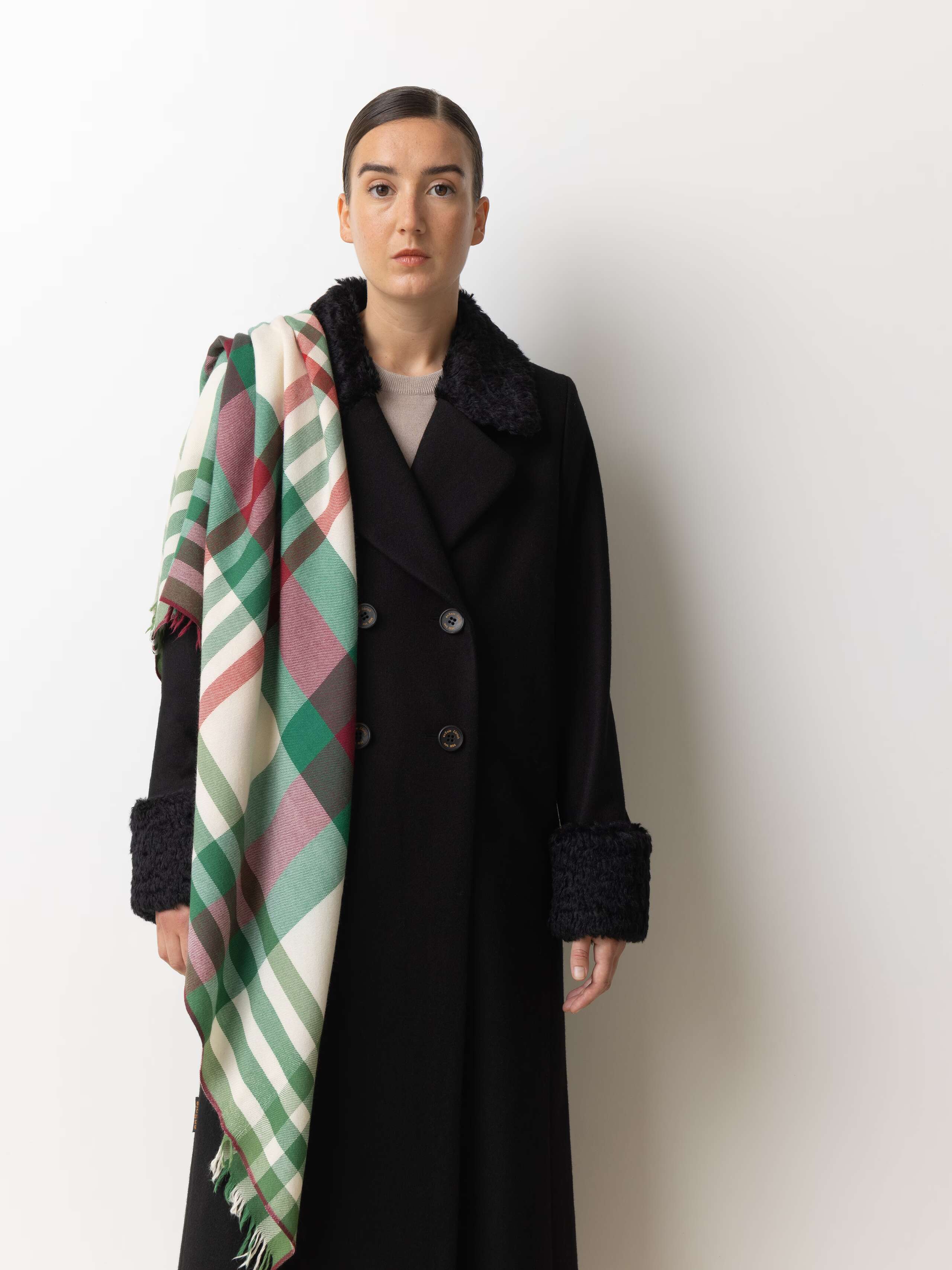 Picture of a female model wearing a black winter coat in combination with a oversized woolscarf in beige featuring a beautiful check pattern in green and red shades