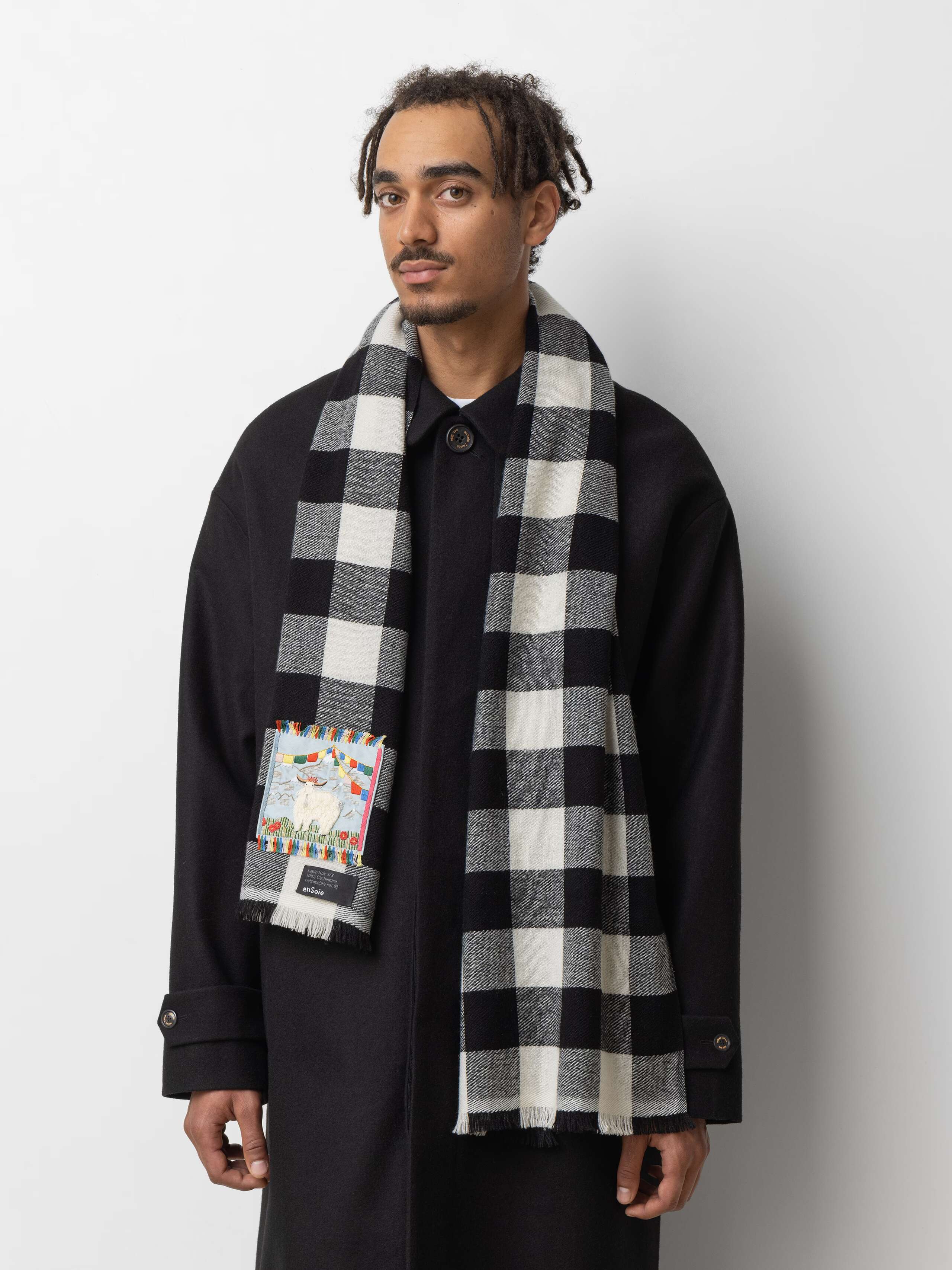 Picture of a male model wearing a black winter coat and a cashmere scarf featuring a black and white check pattern